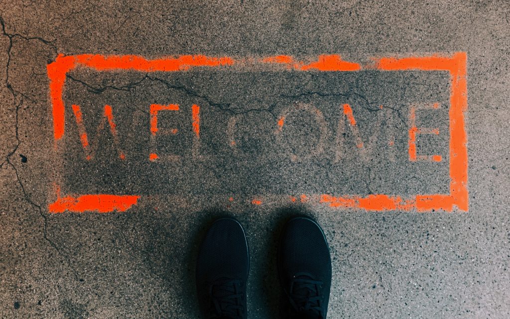 Welcome Wrote In Red Paint On A Concrete Floor With Black Shoes